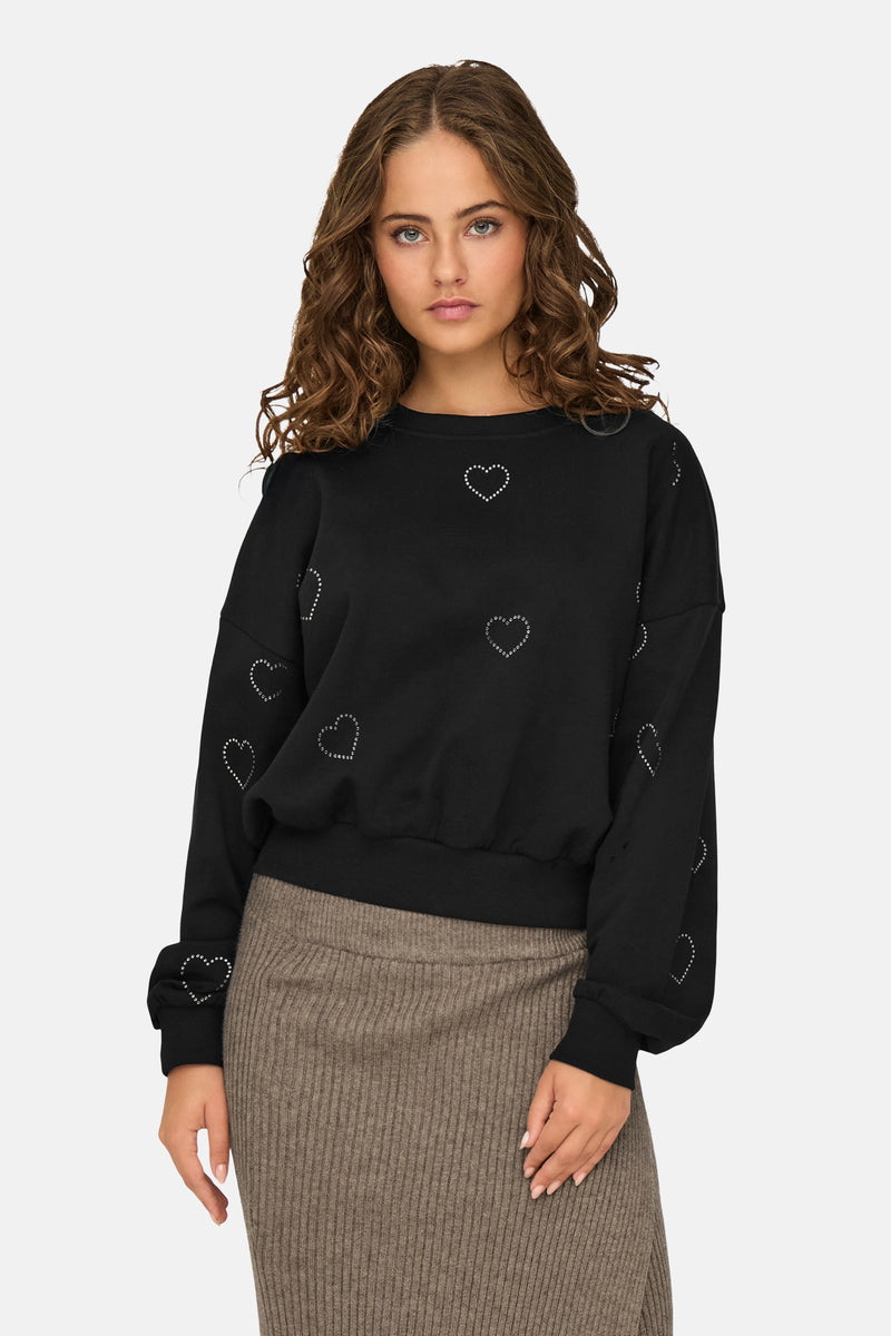 Sweat noir à col rond par ONLY orné de motifs de coeurs argentés, porté avec une jupe côtelée marron.
