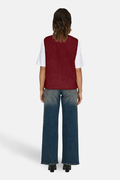 Bordeaux mouwloos vest van ONLY®, gedragen over een wit T-shirt met een verloopje spijkerbroek en zwarte enkellaarsjes.