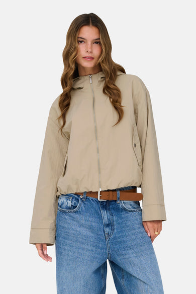 Veste courte beige de ONLY, avec fermeture éclair et portée avec un jean bleu et une ceinture marron.