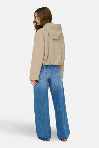 Korte beige jas van ONLY, van achteren gezien, met capuchon en een wijde spijkerbroek.