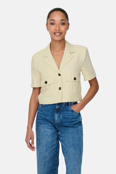 Chemise à manches courtes beige de JDY, avec poches à rabat et boutons foncés, portée avec un jean bleu.