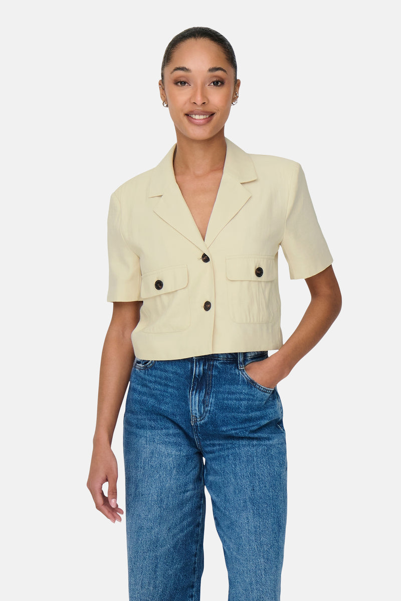 Chemise à manches courtes beige de JDY, avec poches à rabat et boutons foncés, portée avec un jean bleu.