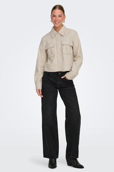 Veste courte écru de ONLY, avec poches à rabat, portée avec un jean noir taille haute et des bottines en cuir noir.
