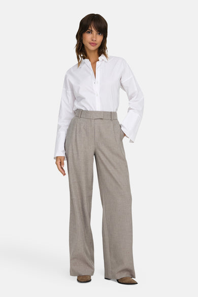 Pantalon de costume beige de ONLY, avec ceinture et coupe ample, porté avec une chemise blanche.
