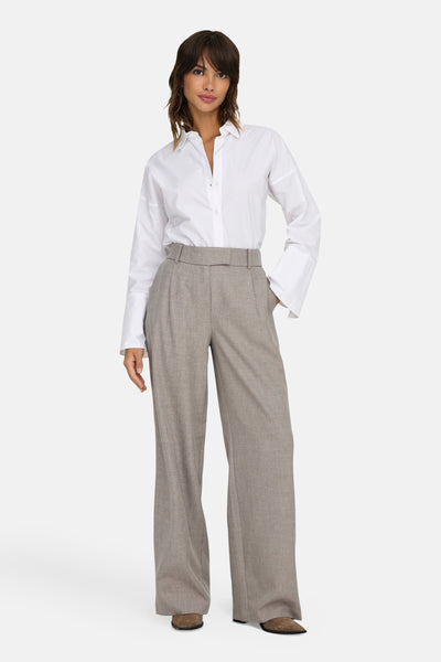 Pantalon de costume beige de ONLY, avec ceinture et coupe ample, porté avec une chemise blanche.
