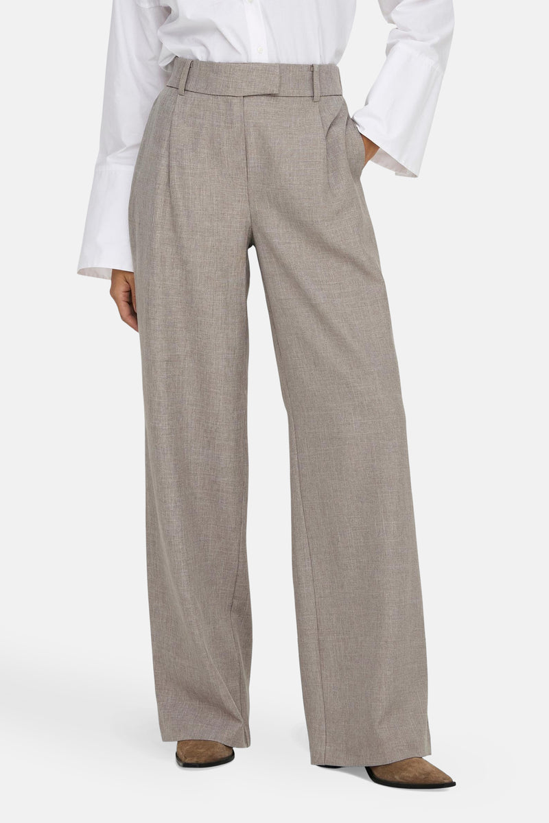 Pantalon de costume beige de ONLY, coupe ample, porté avec une chemise blanche à manches larges.
