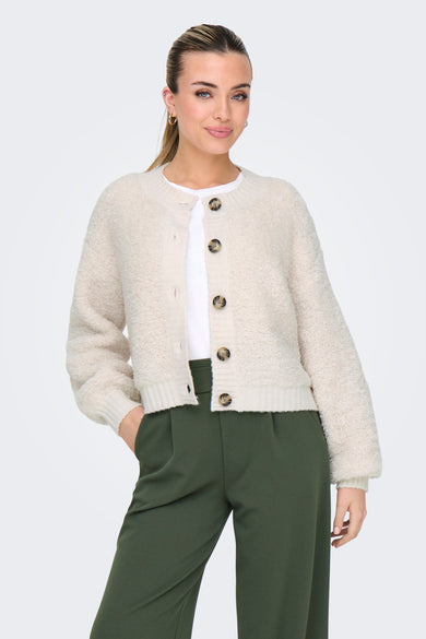 Cardigan écru de JDY, avec boutons marron, porté sur un t-shirt blanc et un pantalon vert olive.
