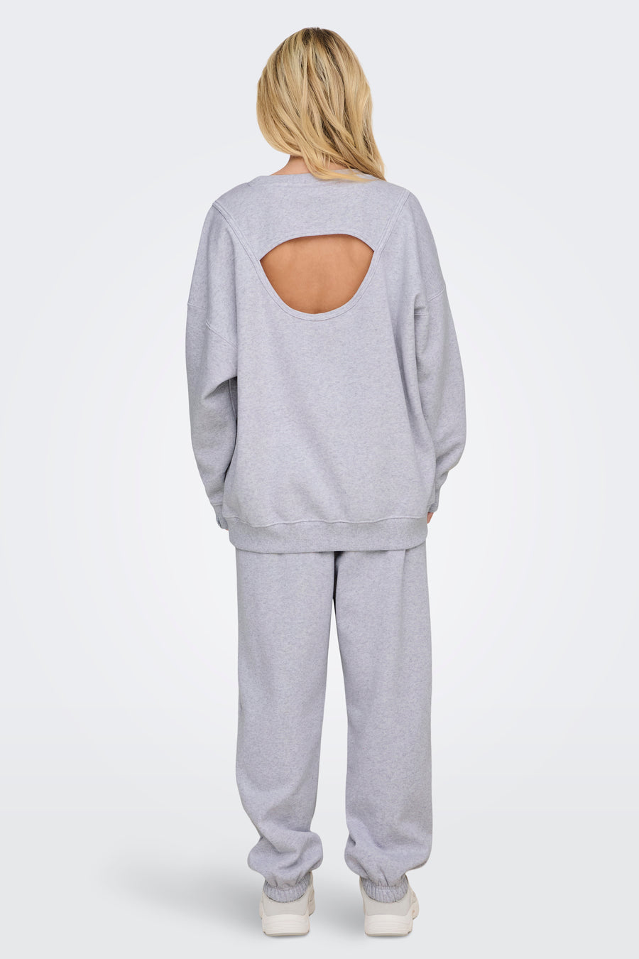Sweat col rond gris de ONLY, avec une découpe dans le dos, porté avec un pantalon de survêtement assorti.