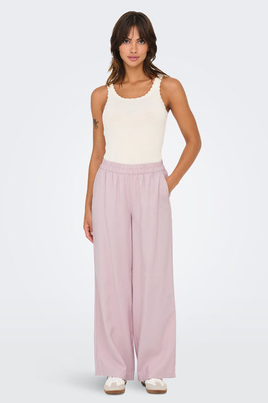 Pantalon rose de ONLY, avec des jambes larges, porté avec un débardeur ivoire côtelé et des baskets.