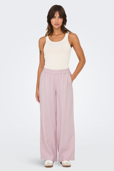 Pantalon rose de ONLY, avec des jambes larges, porté avec un débardeur ivoire côtelé et des baskets.