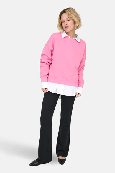 Sweat rose de ONLY®, porté avec une chemise blanche à col et un pantalon noir.