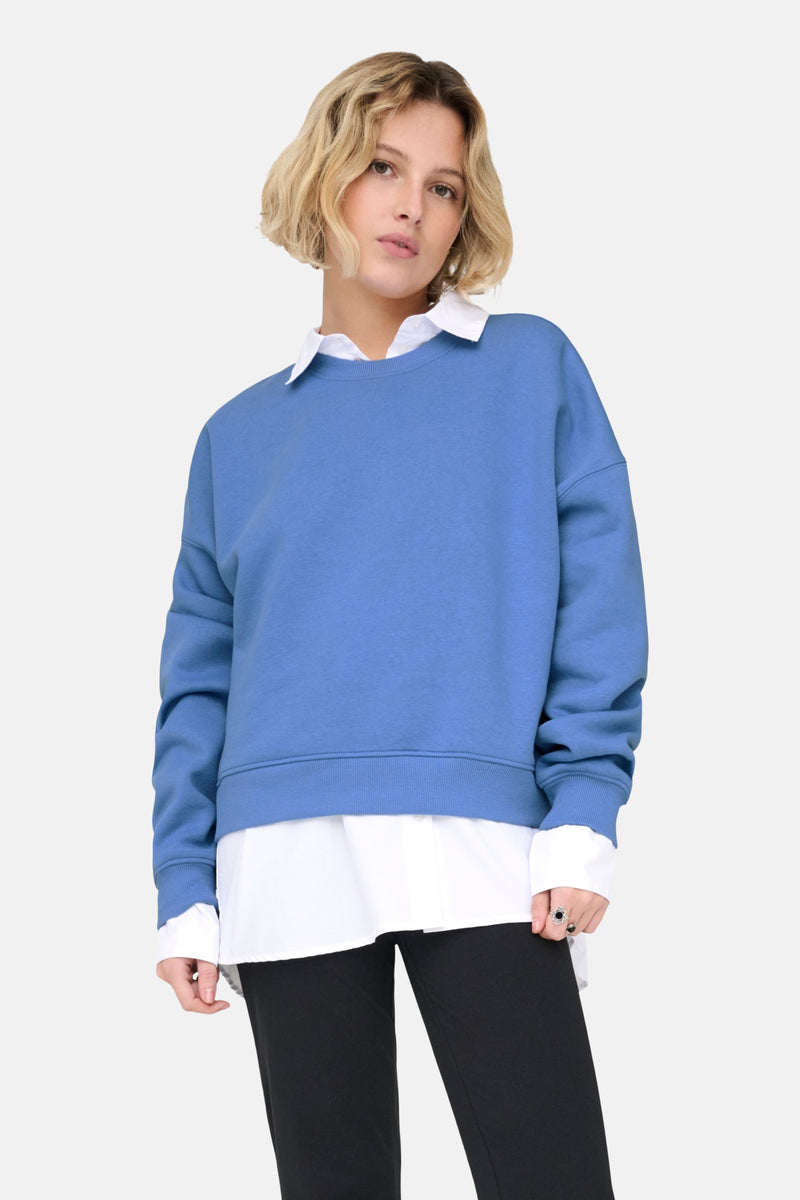Blauwe ONLY trui, gedragen over een wit overhemd, met een zwarte broek en bijpassende hakken.