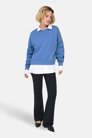 Sweat bleu ONLY, porté sur une chemise blanche, avec un pantalon noir et des chaussures à talons assorties.