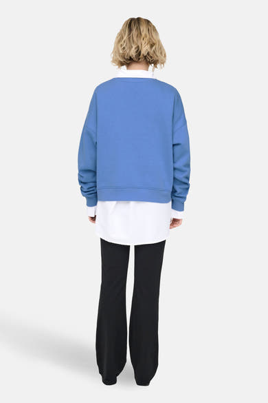 Blauwe trui van ONLY®, gedragen over een wit overhemd en een zwarte wijde broek, achtergezicht.