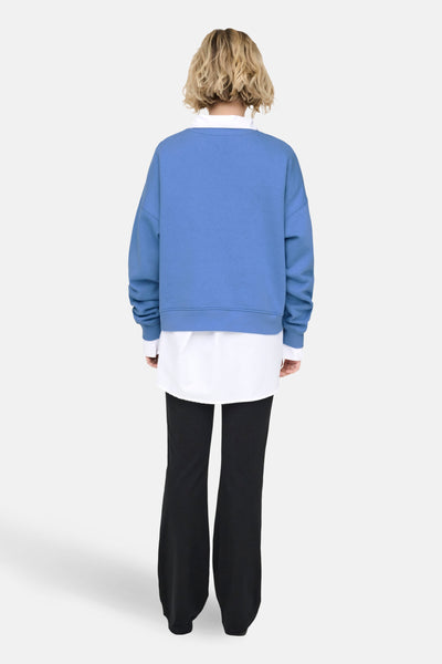 Blauwe trui van ONLY®, gedragen over een wit overhemd en een zwarte wijde broek, achtergezicht.