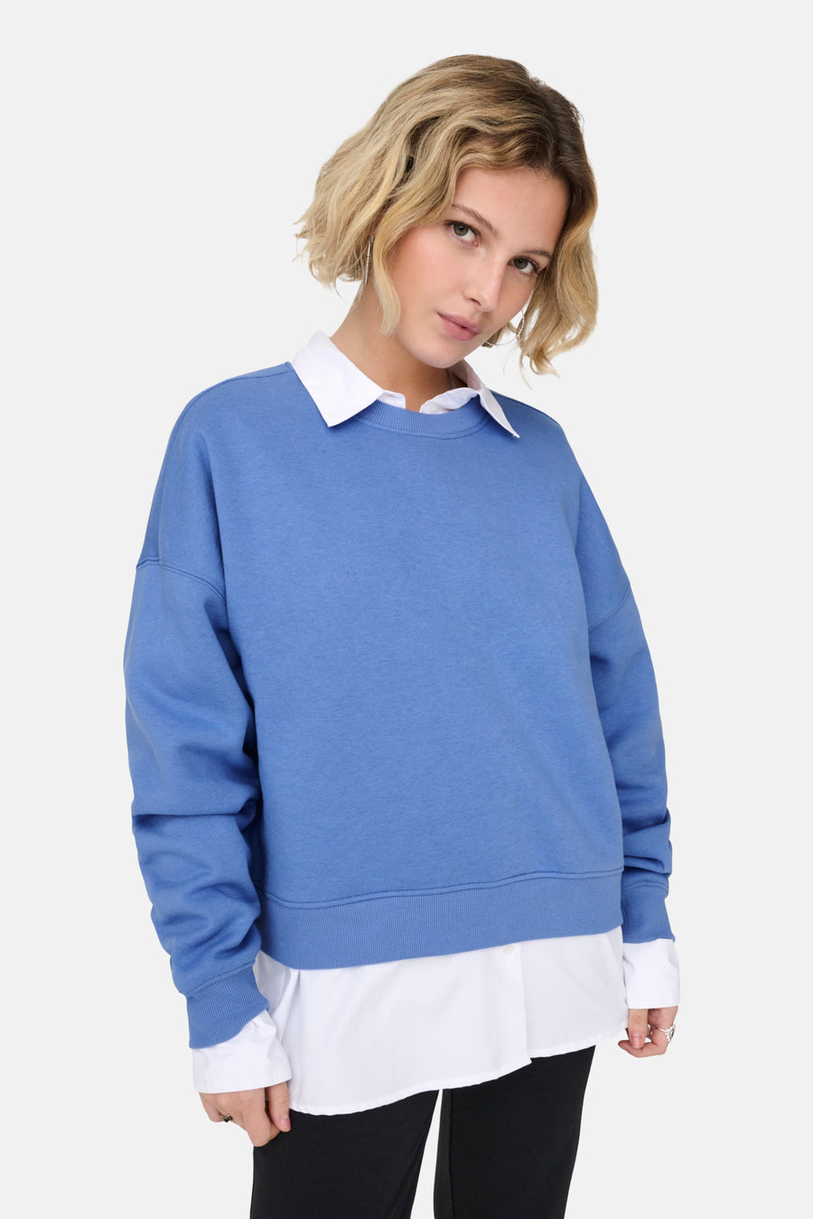 Blauwe trui van ONLY, gedragen over een wit overhemd met kraag, met een zwarte broek.