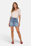 Jupe courte en denim bleu clair de ONLY®, portée avec un t-shirt beige et des chaussures rouges à brides.
