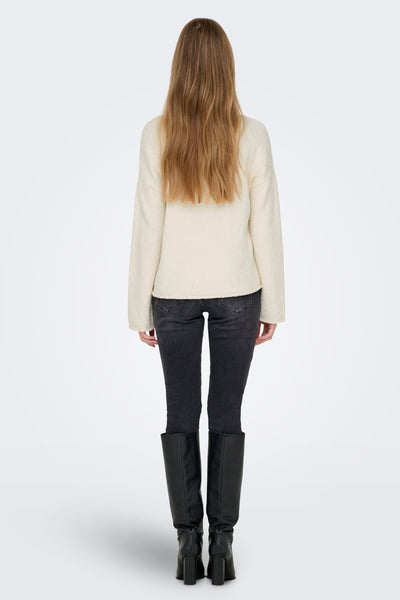 Ronde mouwige beige van ONLY, gedragen met een zwarte jeans en zwarte hoge laarzen.