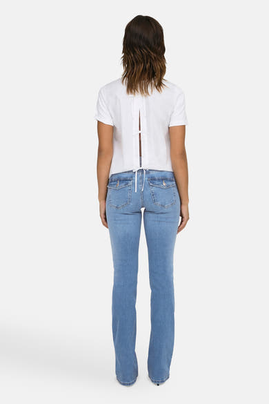 Jean évasé bleu moyen de ONLY®, avec poches plaquées à l'arrière, porté avec un chemisier blanc à dos ouvert.
