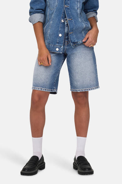 Short en denim bleu moyen de ONLY, porté avec une veste en jean et des mocassins noirs avec des chaussettes blanches.
