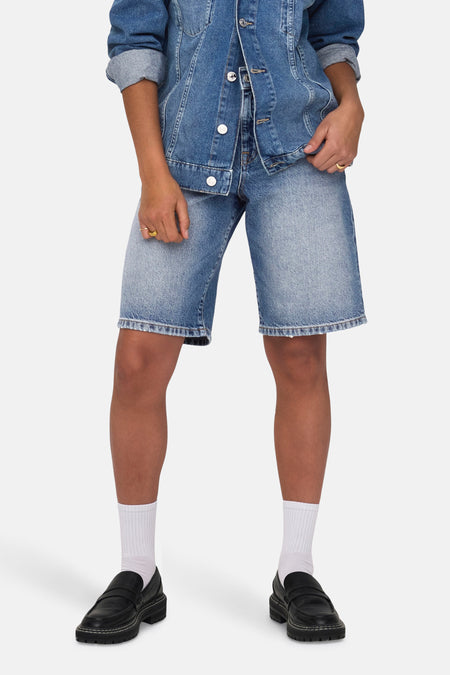 Korte middellange blauwe spijkerbroek van ONLY, gedragen met een spijkerjasje, witte sokken en zwarte loafers.