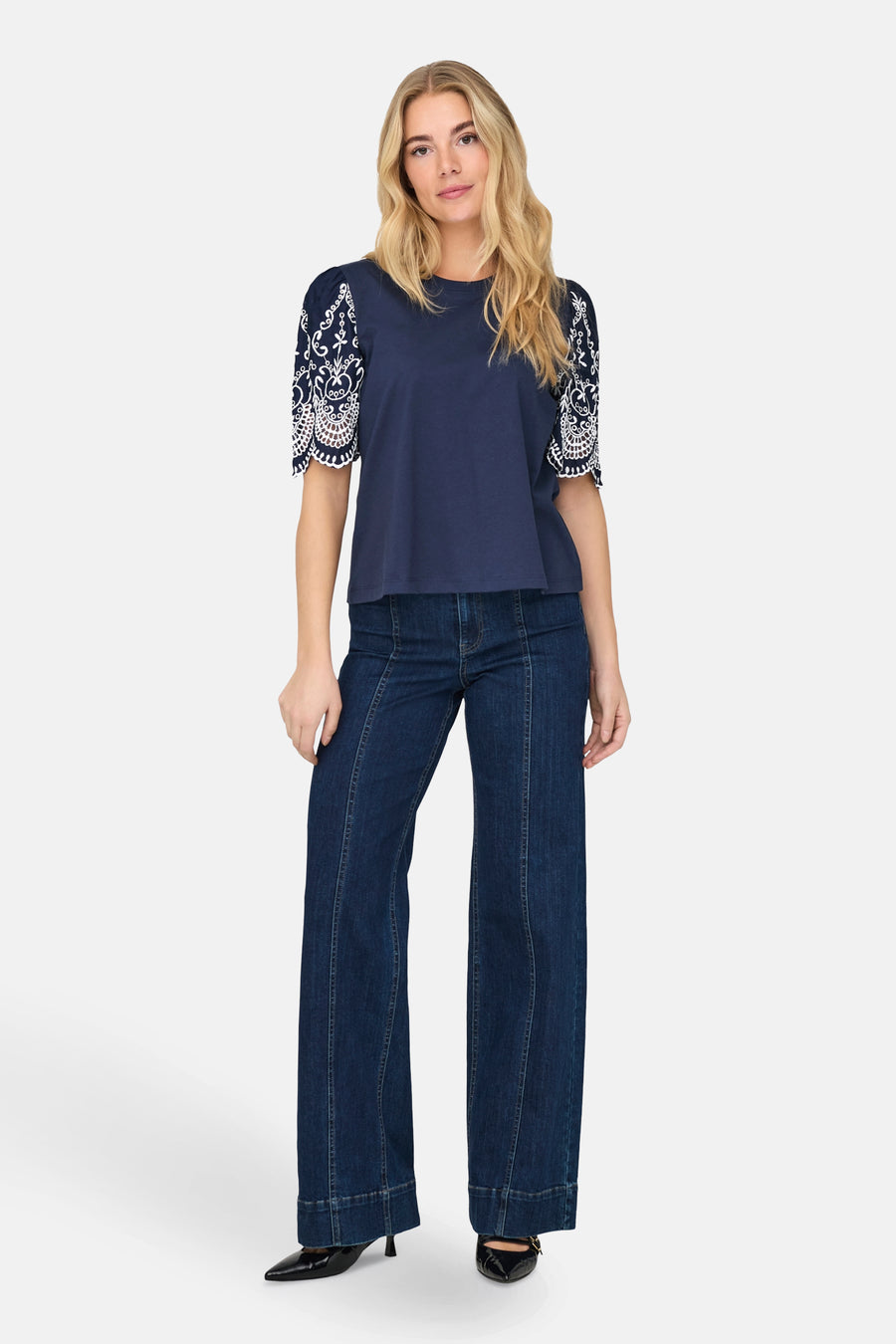T-shirt bleu à manches courtes de JDY, avec broderie blanche décorative sur les manches, porté avec un jean évasé.
