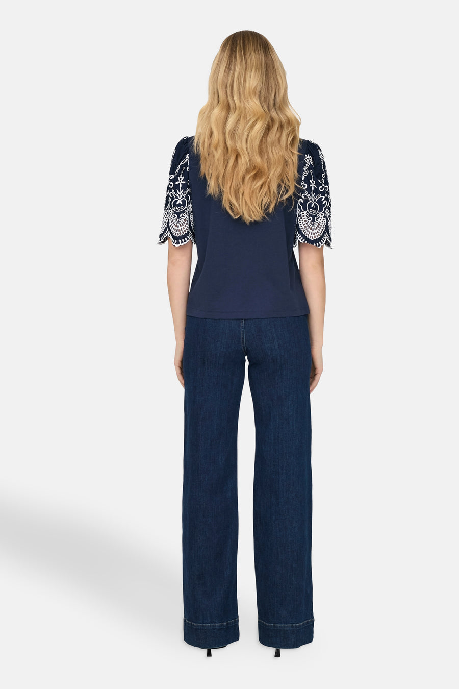 T-shirt bleu à manches courtes de JDY, avec broderie décorative blanche sur les manches, porté avec un pantalon en denim.