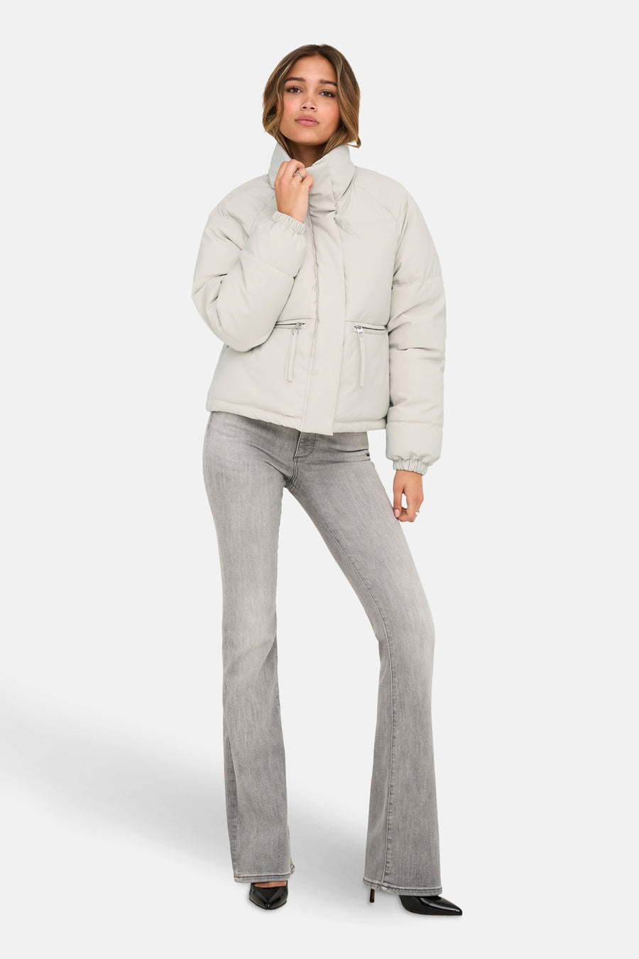 Veste courte beige de JDY, avec poches zippées, portée avec un jean gris évasé et des escarpins noirs.
