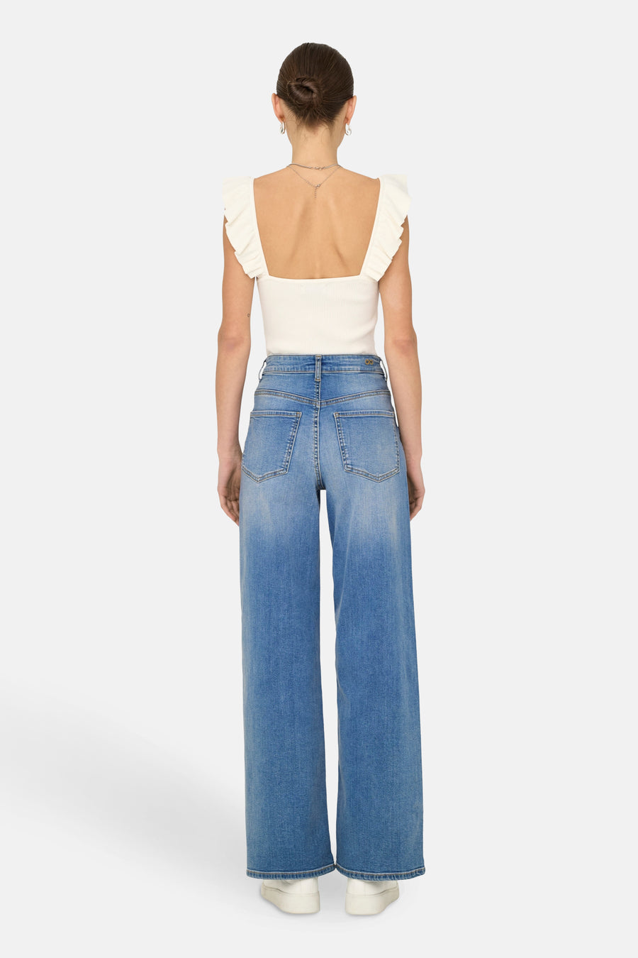 Wijde jeans in middieblauw denim van JDY, achteraanzicht, met een witte top met ruches en witte schoenen.