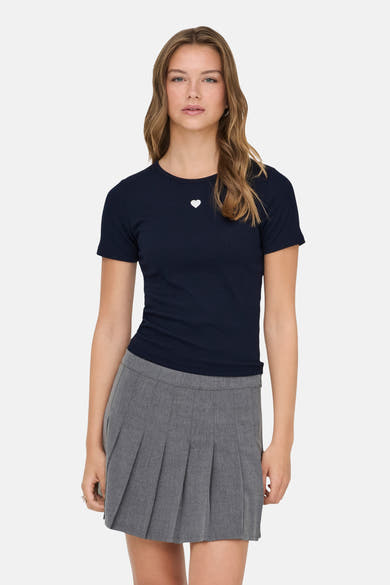 T-shirt bleu marine à manches courtes de ONLY, avec un petit cœur blanc brodé, porté avec une jupe grise plissée.