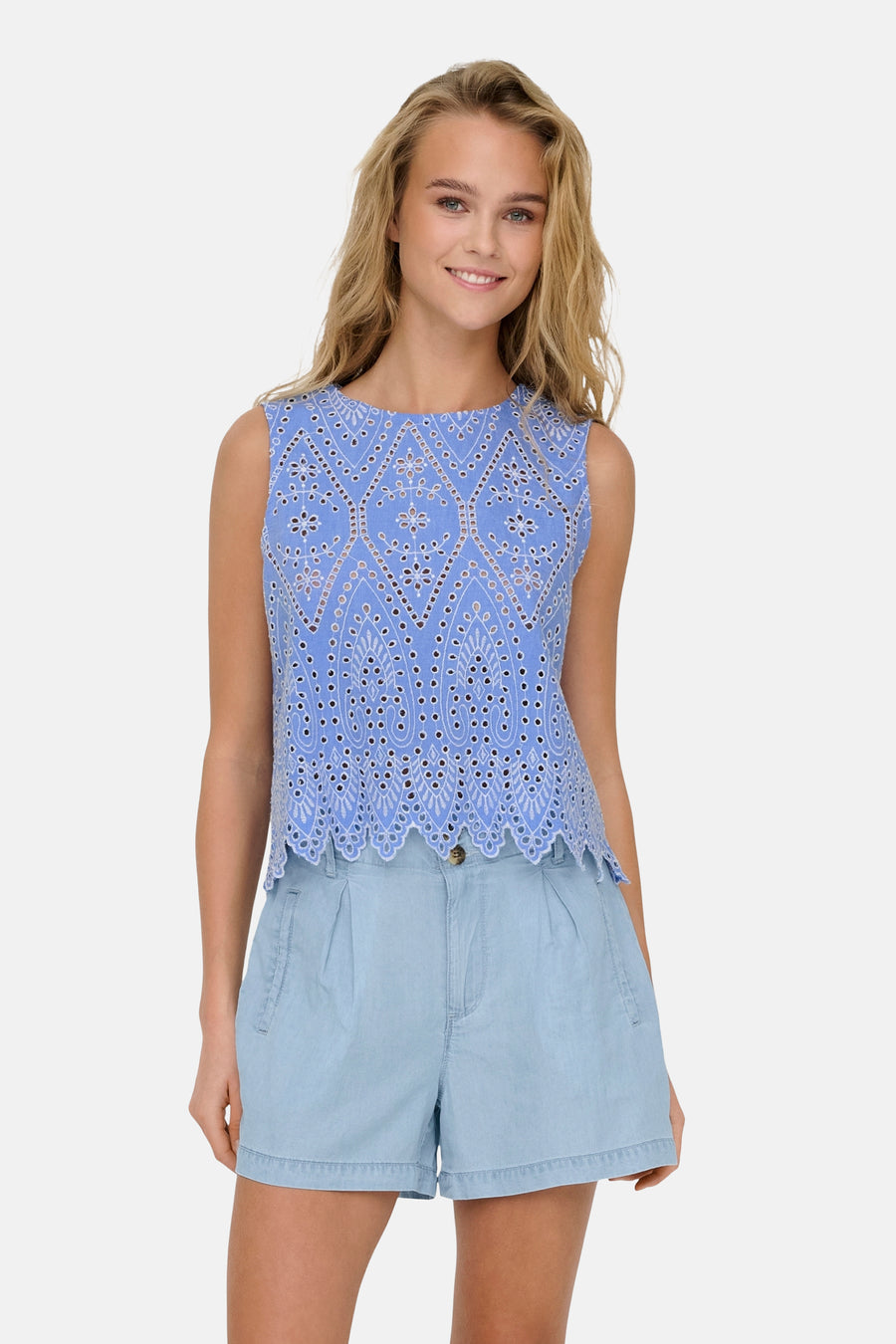 Blouse bleue sans manches de ONLY, avec motif ajouré et détails délicats, portée avec un short bleu clair.
