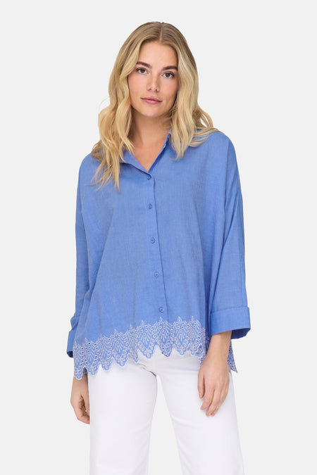 Chemisier bleu de ONLY, avec bordure en dentelle ornementale, porté sur un pantalon blanc.
