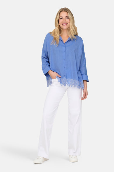 Chemisier bleu de ONLY, avec bordure en dentelle, porté avec un pantalon blanc et des baskets.