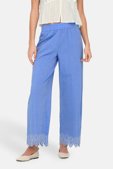 Blauwe broek van ONLY, met geborduurde kanten rand aan de enkels, gedragen met een witte top.
