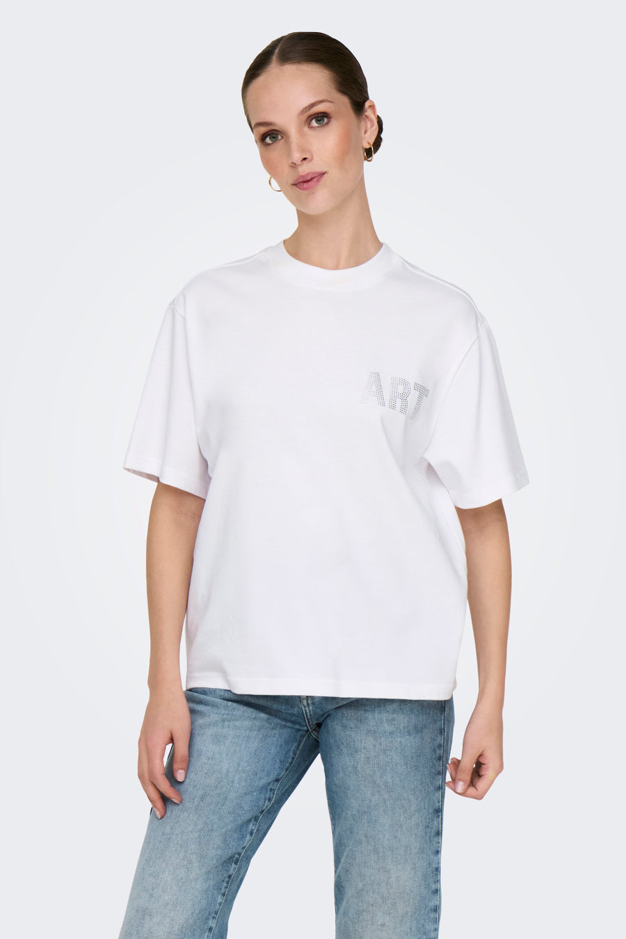 Wit T-shirt met korte mouwen van ONLY, versierd met het woord "ART" in strassteentjes, gedragen met een spijkerbroek.