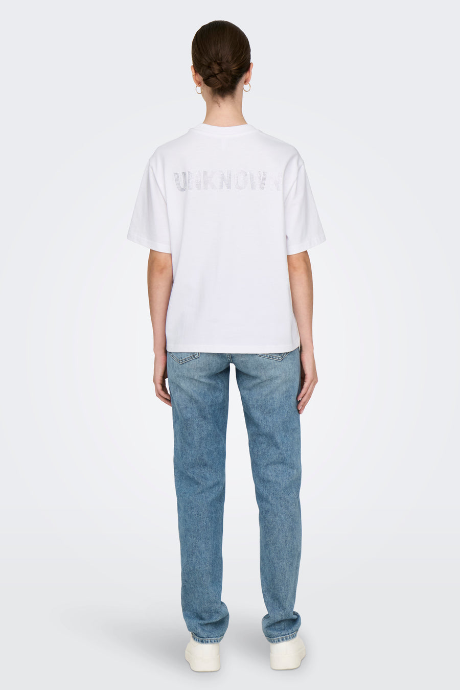 Wit T-shirt met korte mouwen van ONLY, met opdruk op de rug, gedragen met een lichtblauwe jeans en witte schoenen.