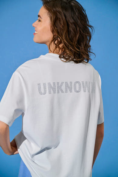 Wit T-shirt met korte mouwen van ONLY, versierd met strass dat het woord "Unknown" vormt, gedragen met een blauwe broek.