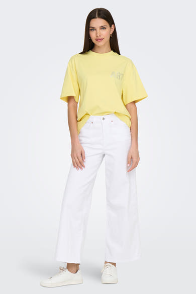 Gele T-shirt met korte mouwen van ONLY, versierd met zilveren strassteentjes, gedragen met een witte broek en witte sneakers.