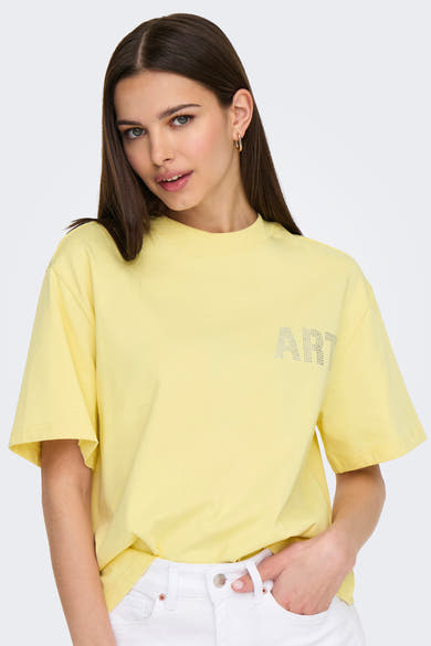 Gele T-shirt met korte mouwen van ONLY, met het woord "ART" in strassteentjes, gedragen met een witte jeans.
