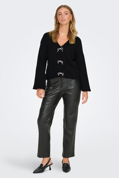 Cardigan noir de ONLY, orné de nœuds décoratifs, porté avec un pantalon en similicuir et des escarpins noirs.
