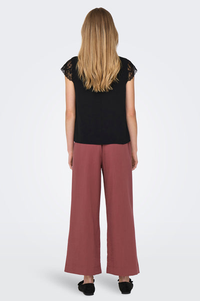 Zwarte korte mouw T-shirt van ONLY, met dentelle mouchen en gedragen met een ruime roze broek.