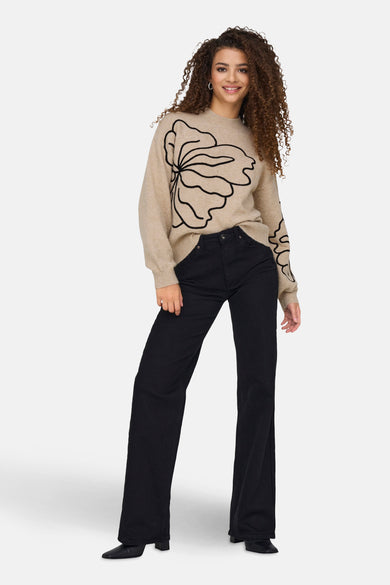 Beige ronde hals trui van JDY met zwart bloemenpatroon op de voorkant, gedragen met een zwarte broek.