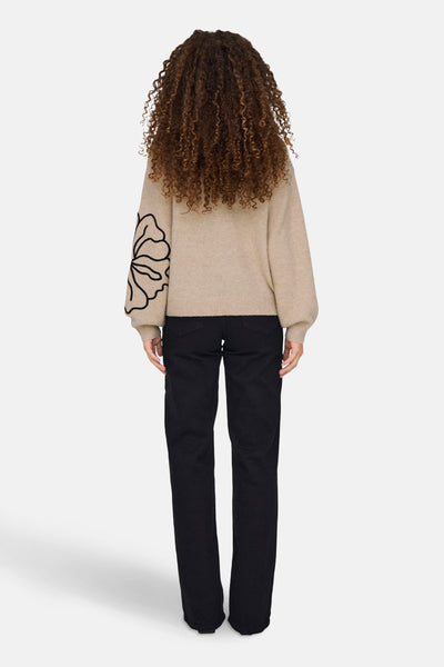 Beige ronde hals trui van JDY, met een zwart bloemenpatroon op de mouw, gedragen met een zwarte jeans.
