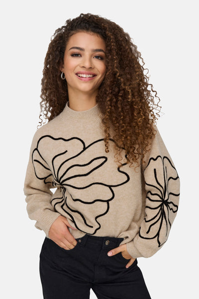 Pull col rond beige de JDY avec motif floral noir, porté avec un jean foncé.