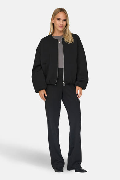Veste courte noire de ONLY, avec une fermeture éclair argentée, portée avec un pantalon noir et un t-shirt gris.
