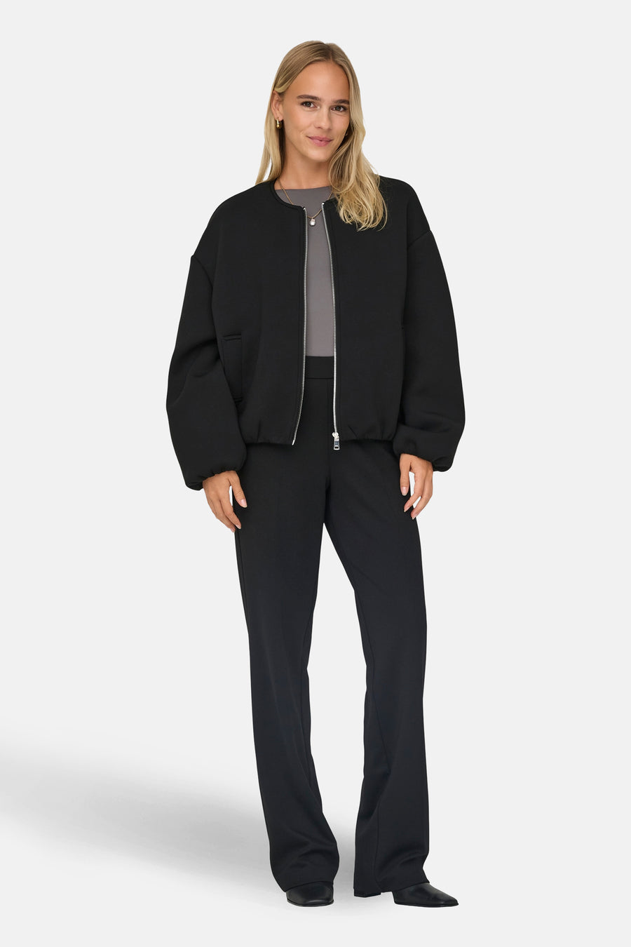 Veste courte noire de ONLY, avec une fermeture éclair argentée, portée avec un pantalon noir et un t-shirt gris.