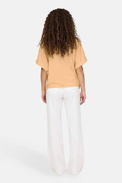 Oranje T-shirt met korte mouwen van ONLY®, gedragen met een witte broek met hoge taille, achtergezicht.