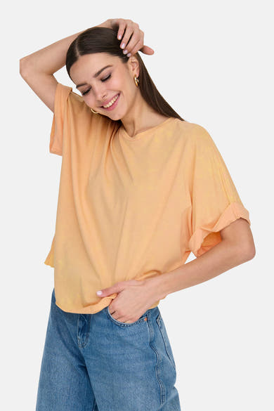 Oranje T-shirt met korte mouwen van ONLY®, gedragen met een blauwe spijkerbroek en gouden oorbellen.