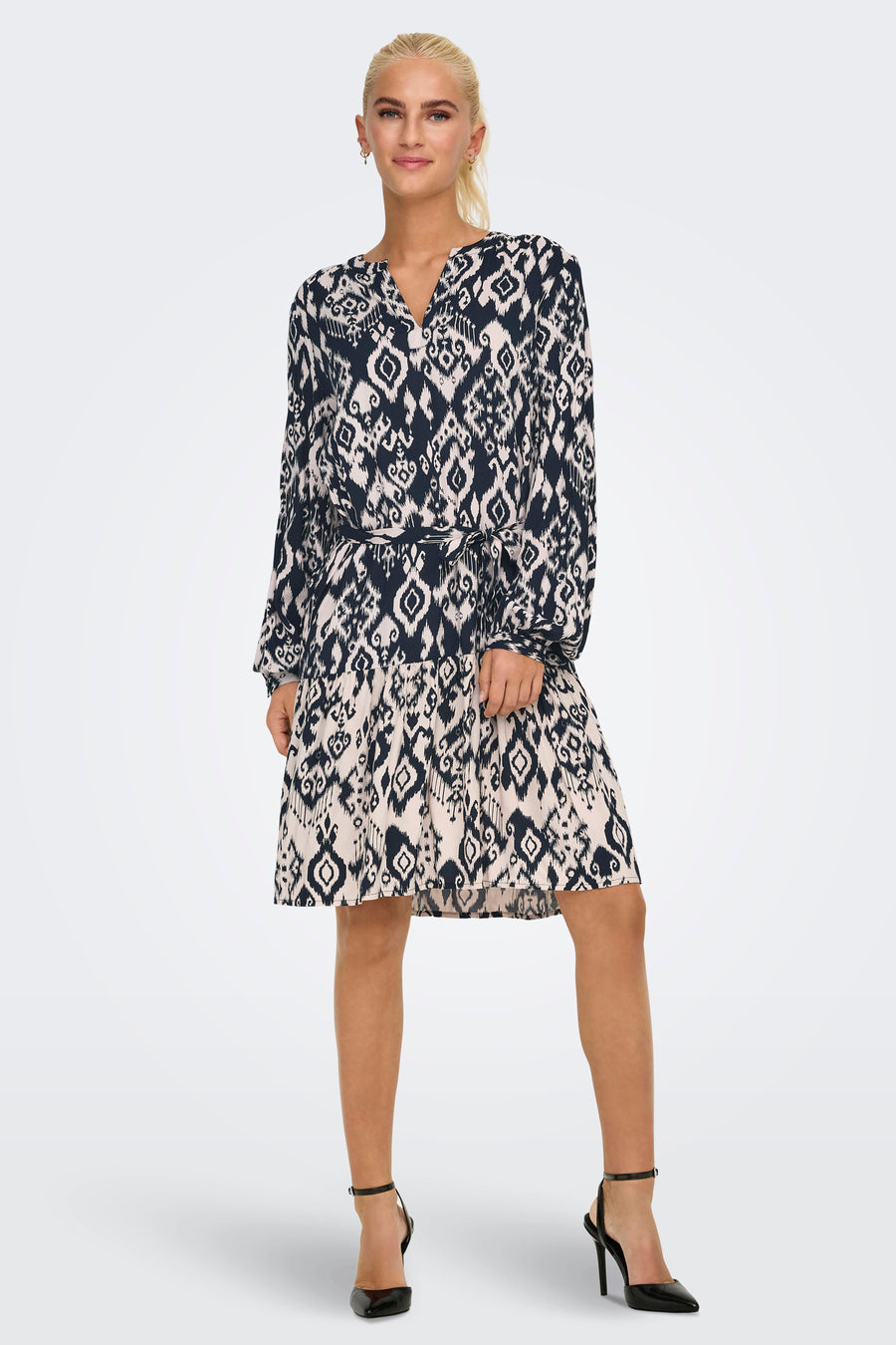 Robe noire à manches longues de JDY, avec motif losange, ceinture nouée et chaussures à talons noirs.
