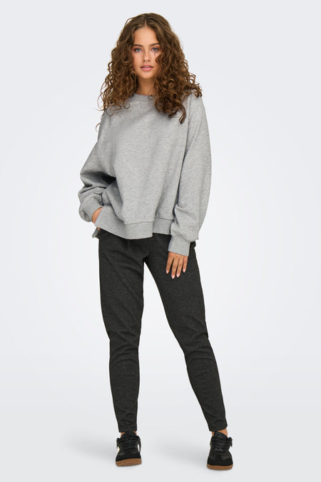 Sweat gris de ONLY, avec des détails de strass sur les manches, porté avec un pantalon à motif chiné et des baskets noires.

